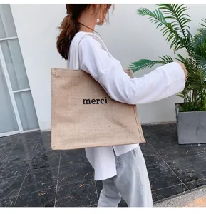 Casual burlap tote bag with merci print carried by a model in outdoor setting
