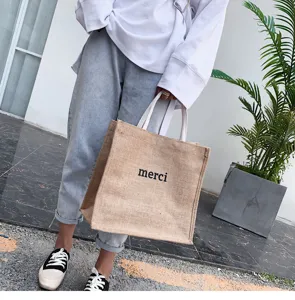 Minimalist jute tote bag with 'merci' print carried in a casual street setting
