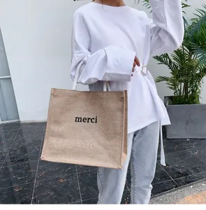 Casual large capacity jute tote bag with 'merci' print held by model in white top