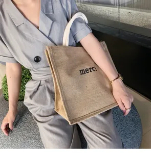 Detailed view of a natural burlap tote bag featuring a black merci print and white handles