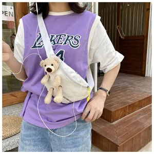Outdoor street style detail of white canvas chest bag with cute plush bear attachment