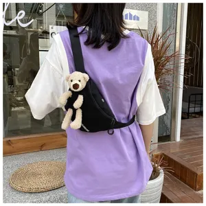 Detail view of a casual black canvas chest bag with a cute plush teddy bear accessory