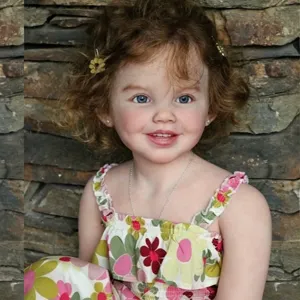 Realistische Reborn-Kleinkindpuppe mit lockigem rotem Haar und blumigem Kleid Detail.