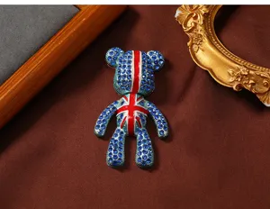Gedetailleerd beeld van een teddybeer broche met blauwe kristallen en Union Jack vlagpatroon