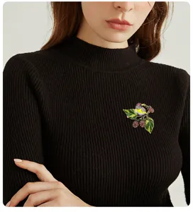 Close-up of vintage magpie and strawberry brooch pinned on a black ribbed sweater.