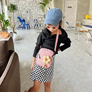Niña con un mini bolso bandolera a cuadros rosa con detalle de flor amarilla.