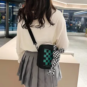 Detalle de un bolso bandolera japonés negro con cuadros verdes y muñeca linda