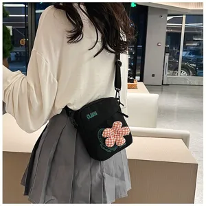 Mujer con bolso bandolera negro con detalle de flor a cuadros y texto impreso.