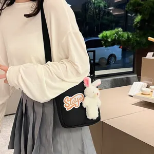 Detalle de un bolso bandolera negro con un lindo colgante de conejo de peluche blanco.