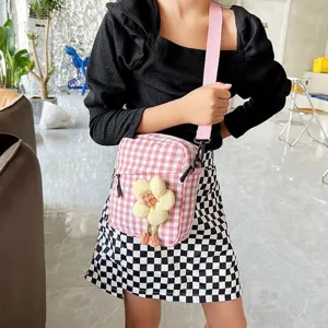 Niña luciendo un mini bolso bandolera de cuadros rosas con una flor de peluche decorativa.