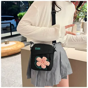 Primer plano de un bolso bandolera negro de estilo estudiantil con flor a cuadros.