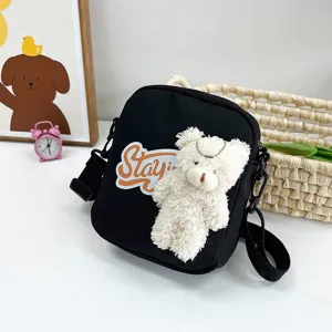 Vista detallada de un bolso bandolera de nailon negro con un tierno oso de peluche