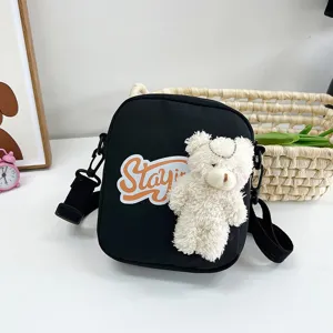 Primer plano de bolso bandolera de nailon con un oso de peluche blanco y parche naranja
