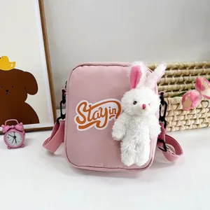 Detalle de bolso bandolera de lona rosa con conejo de peluche 3D y texto Stay in
