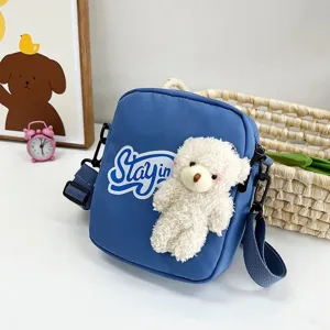 Primer plano del bolso bandolera de nailon azul con adorable osito de peluche blanco.