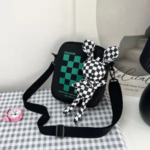 Detalle de bolso bandolera negro con cuadros verdes y un adorable accesorio de conejo