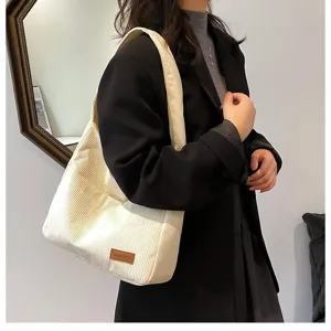Large white corduroy tote bag shown from side view on model's shoulder in black blazer