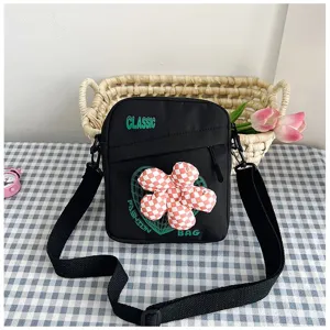 Vista detallada del bolso bandolera de lona negra con decoración de flores a cuadros rojos en 3D