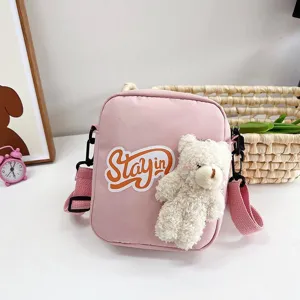 Detalle de un bolso bandolera de nailon rosa con un oso de peluche y parche 'STAY in'