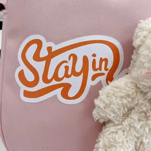 Primer plano de bolso bandolera de nailon rosa con colgante de oso de peluche y estampado