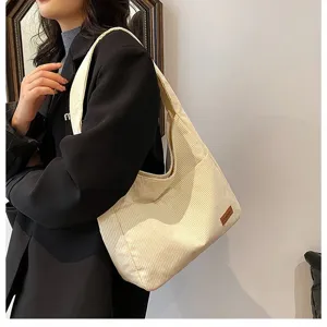 Macro view of a stylish large off-white corduroy shoulder tote bag worn by a female model