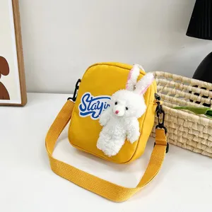 Detalle de bolso bandolera amarillo con un tierno conejo de peluche e inscripción