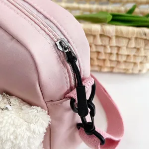 Detalle de bolso bandolera de nailon rosa con un lindo colgante de oso y cremallera