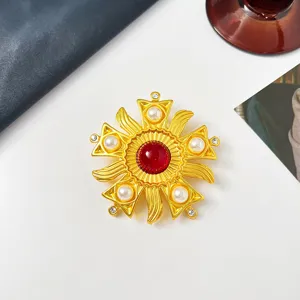 Detailansicht einer goldenen Vintage-Sonnenbrosche mit rotem Zentrum und Perlen