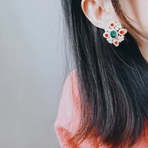 Close-up of vintage baroque geometric earrings with green and red gemstones on ear.
