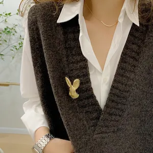 Detailed close-up of a vintage golden rabbit brooch pinned to a dark knit sweater vest.