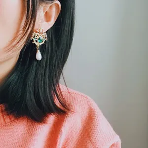 Detail view of vintage baroque gold earrings with green gem and pearl drop on model