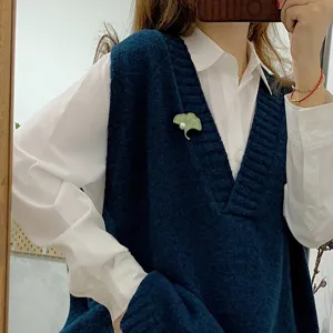 Close-up of a vintage green ginkgo leaf brooch with a white pearl on a navy blue knitted vest.