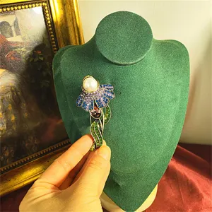 Dettaglio spilla a fiore vintage con perla e strass colorati su supporto verde.