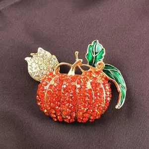 Close-up of a retro pumpkin brooch with red rhinestones and green enamel leaves.