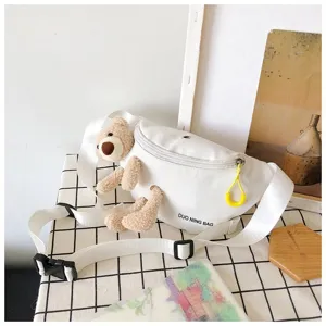 Close-up detail of a white canvas waist bag featuring a cute plush teddy bear decoration