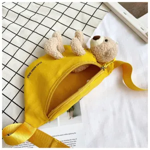Close-up detail of a yellow canvas waist bag with a cute plush teddy bear decoration.