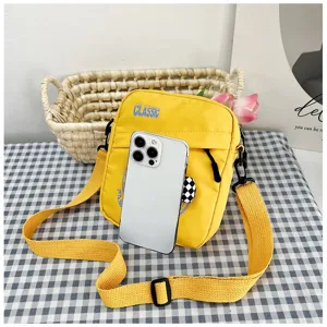 Bolso bandolera pequeño de lona amarilla junto a un móvil para ver el tamaño.