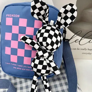 Vista detallada del bolso bandolera de lona azul con colgante de muñeco conejo a cuadros