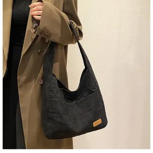 Side view detail of a stylish black corduroy tote bag paired with a classic brown trench coat