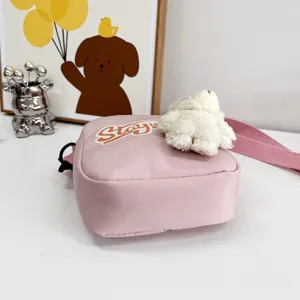 Vista detallada de un bolso bandolera de nailon rosa con un lindo oso de peluche blanco.