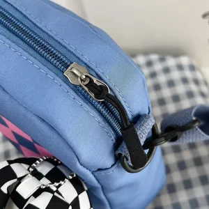 Primer plano de la cremallera del bolso azul con colgante de peluche a cuadros.