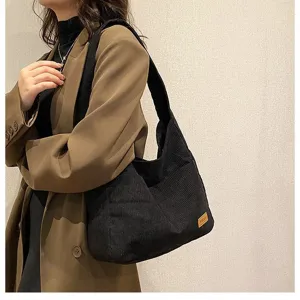 Close-up of a black corduroy tote bag being worn by a model in a stylish brown blazer