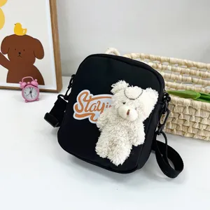 Detalle de bolso bandolera de nailon negro con osito de peluche y correa a la moda.
