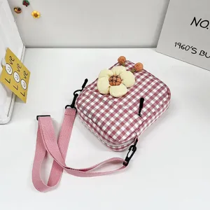 Primer plano de un mini bolso bandolera rosa de cuadros con una linda flor de peluche.