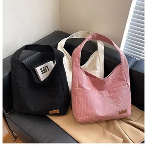 Close-up of large corduroy tote bags in black, pink, and white on a leather sofa