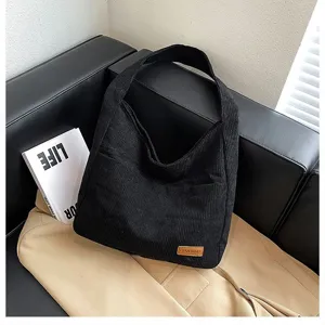 Close-up of black corduroy tote bag showing ribbed texture and stylish leather patch