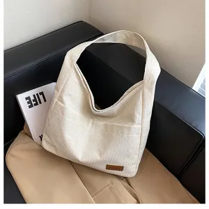 Detailed view of a cream-colored corduroy tote bag displayed on a black leather sofa