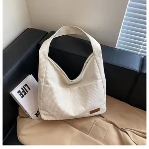 Close-up of a beige corduroy tote bag with a ribbed texture and leather logo patch.