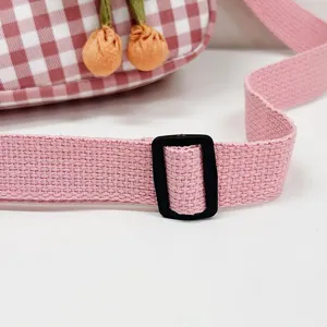 Primer plano de la correa rosa tejida con hebilla negra de un mini bolso de cuadros.