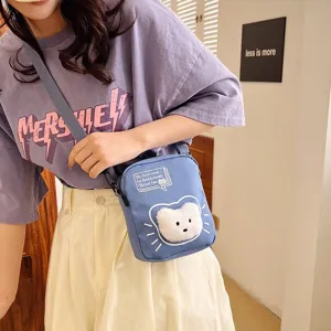 Primer plano de un bolso bandolera de nailon azul con un oso de peluche decorativo.
